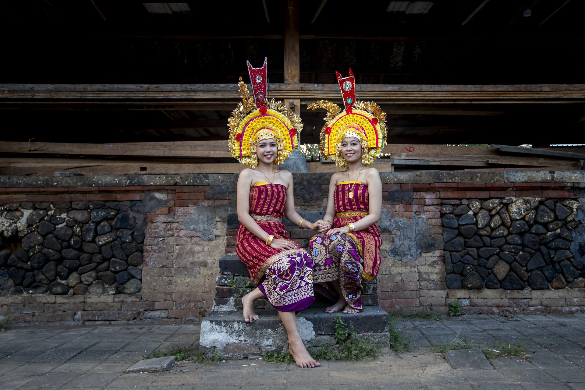 Two women in traditional Balinese ceremonial dress and gold headdresses seated on temple steps